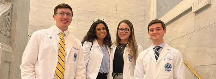Four medical students, two male, two female, stand next to each other wearing their white coats
