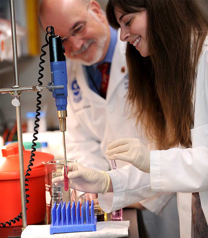 Two researchers in white coats working on lab equipment.