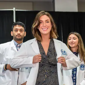 A smiling medicine student wears his white coat for the first time.