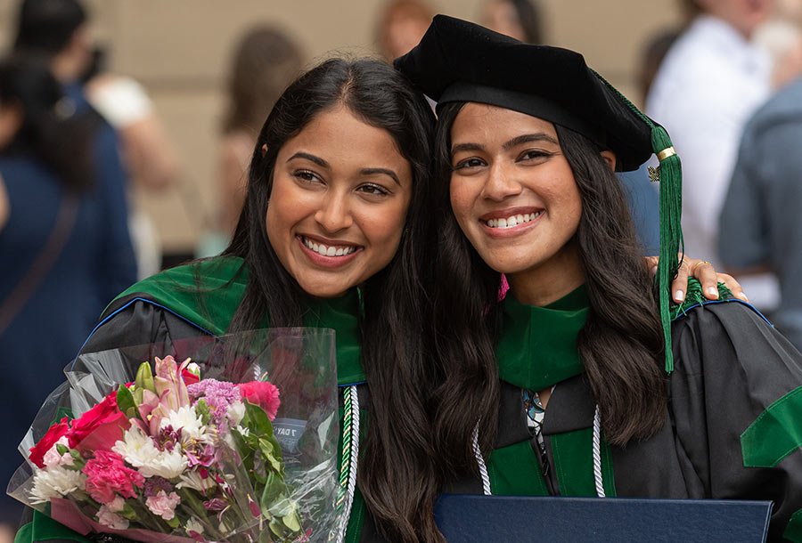 strategic-plan-2025-03 Two graduates hold flowers as they pose for a photogragh.
